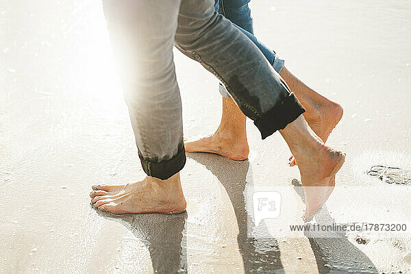 Mature man and woman walking barefoot on shore at beach
