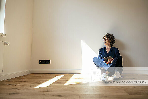 Smiling real estate agent with tablet PC sitting on floor at home