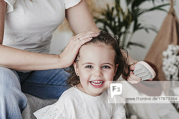Mother brushing cute daughter's hair at home