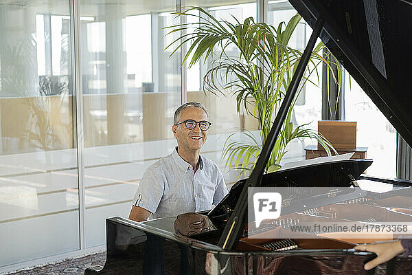 Smiling mature businessman playing piano in office