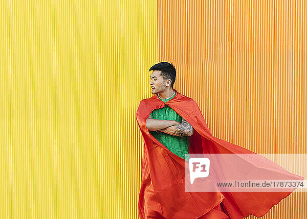 Nachdenklicher junger Mann mit rotem Superheldenumhang steht vor der Wand