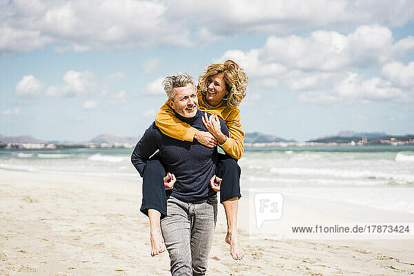 Mature man giving piggyback ride to woman on shore at beach