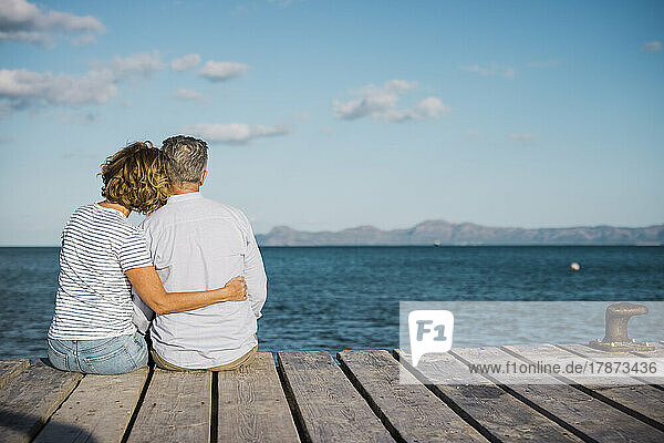 Mature couple spending time together sitting on jetty looking at sea