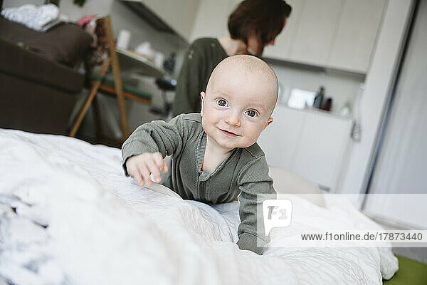 Smiling baby boy crawling on blanket with mother in background at home