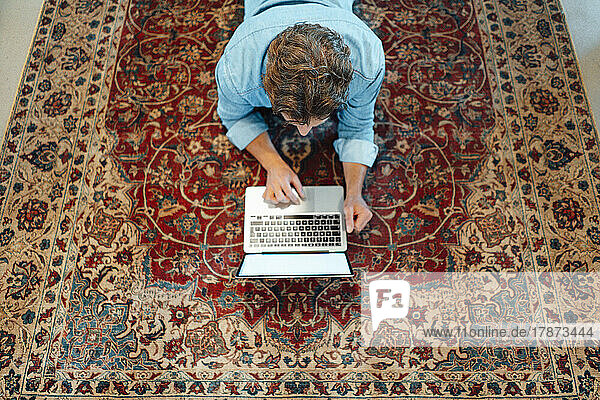 Businessman lying on carpet using laptop in office