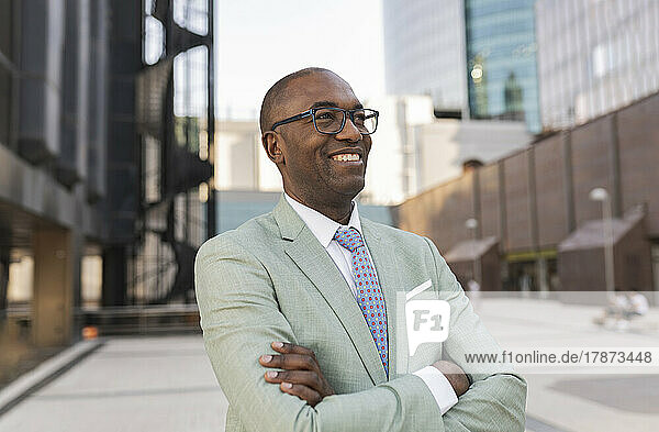 Happy businessman with arms crossed standing at financial district
