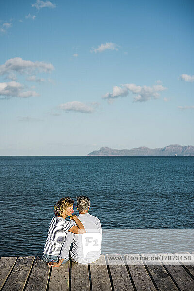 Reife Frau und Mann sitzen auf dem Steg und schauen aufs Meer