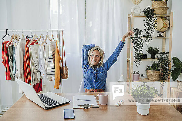 Smiling businesswoman with arms raised sitting at desk in home office