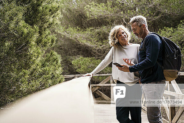 Happy woman with man using smart phone at footbridge