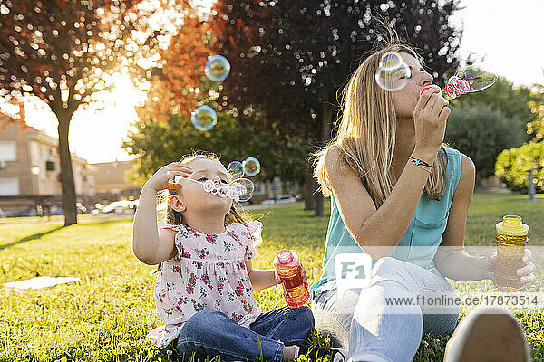 Mother and daughter blowing bubbles sitting at park