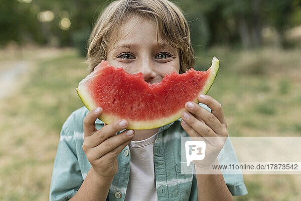 Boy holding slice of watermelon in front of face