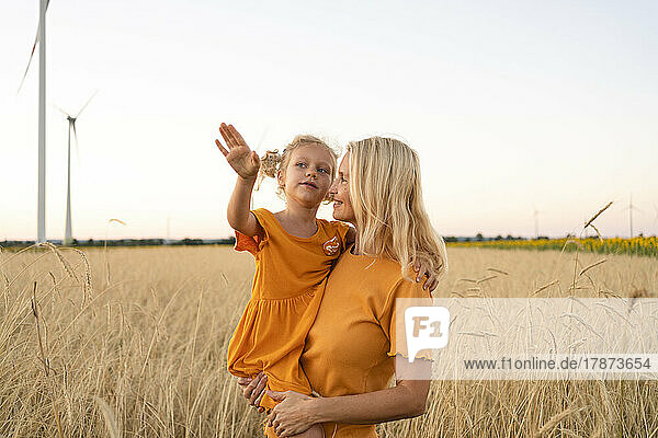 Smiling woman carrying daughter gesturing in wheat field