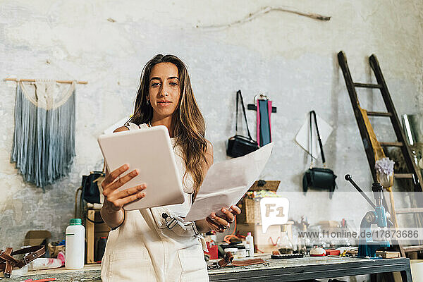 Modedesigner hält Papier in der Hand und schaut auf den Tablet-PC