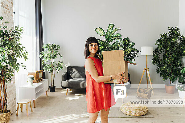 Lächelnde Frau trägt eine Kiste im Wohnzimmer