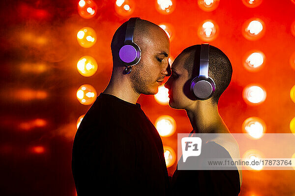 Affectionate couple with headphones by red illuminated lighting