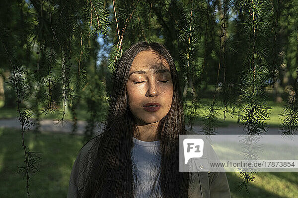 Frau mit geschlossenen Augen steht an einem sonnigen Tag im Park