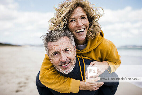 Glücklicher Mann gibt Frau am Strand Huckepackfahrt