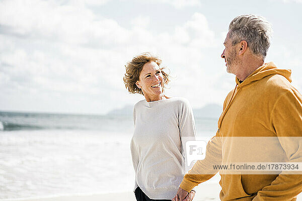 Lächelnde reife Frau mit Mann Händchen haltend am Strand
