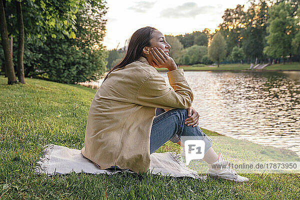 Woman sitting with hand on chin by lake at park