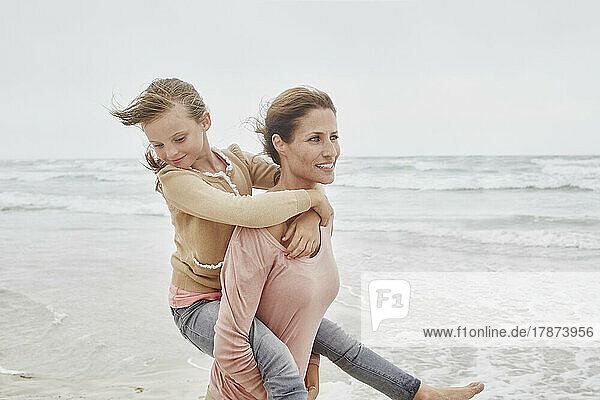 Mother walking on the beach carrying daughter piggyback