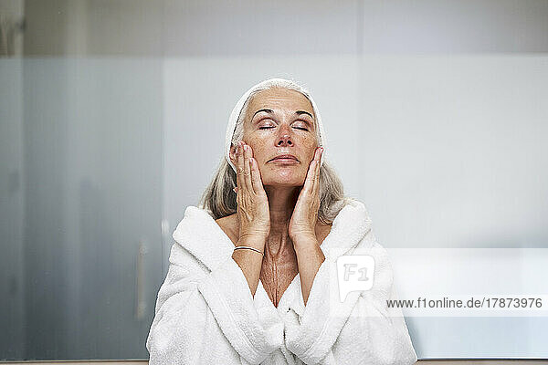 Frau mit geschlossenen Augen berührt Gesicht im Badezimmer