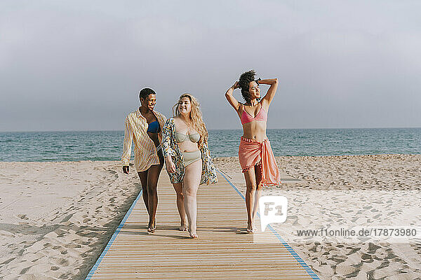 Multiracial friends walking on boardwalk in front of sea at beach