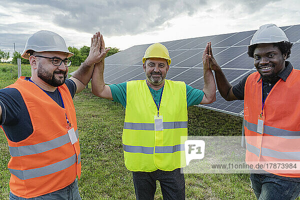 Smiling engineers giving high five to each other at solar power station