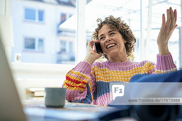 Smiling woman talking on mobile phone sitting at home