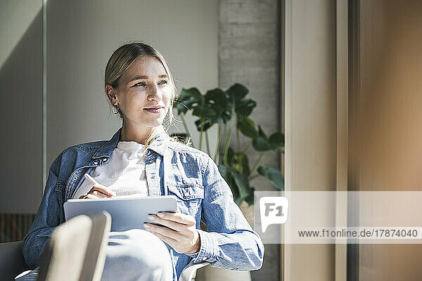 Contemplative businesswoman with tablet PC sitting in office