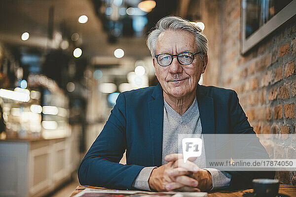 Smiling businessman with hands clasped in cafe