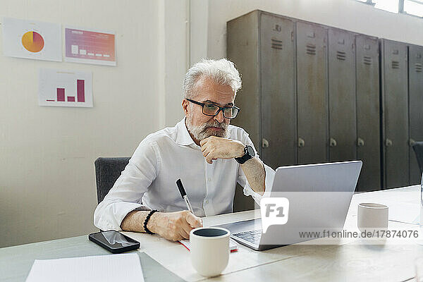 Thoughtful businessman looking at laptop in office