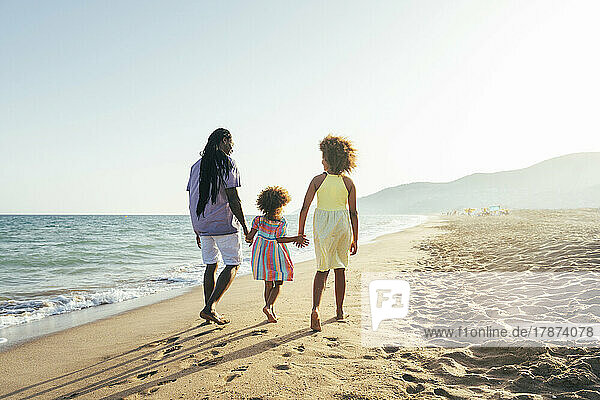 Man with daughters walking at beach on sunny day