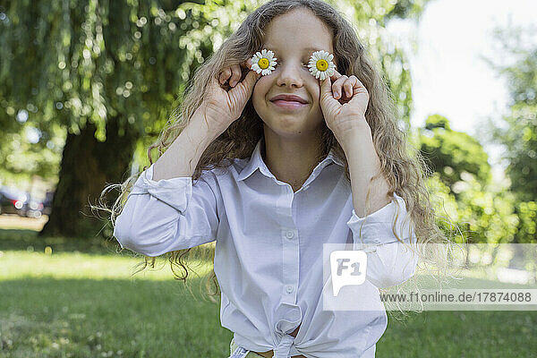 Smiling girl covering eyes with chamomile flowers