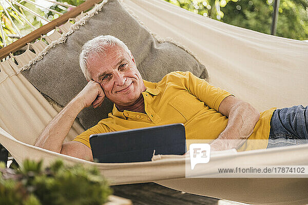 Glücklicher Mann mit Tablet-PC in der Hängematte liegend