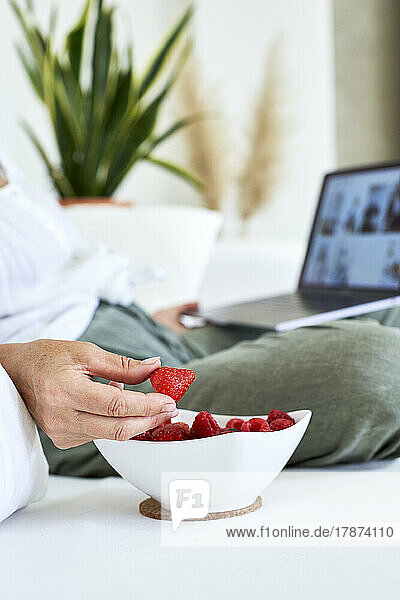 Woman holding strawberry using laptop at home