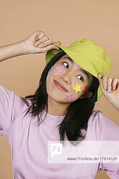 Smiling young woman with stars on face holding yellow bucket hat