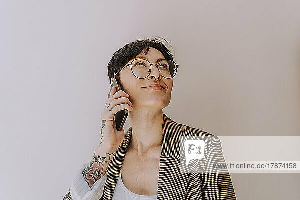 Smiling businesswoman talking on phone in front of wall