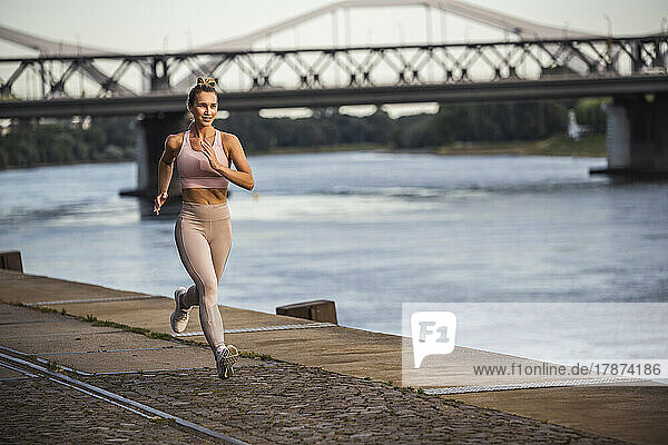 Smiling young woman jogging by river at promenade