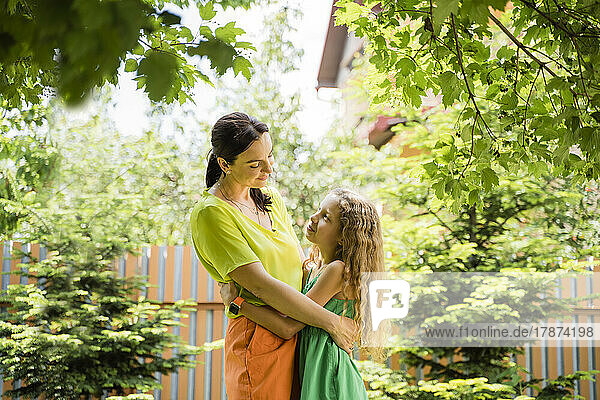 Smiling woman embracing daughter at back yard