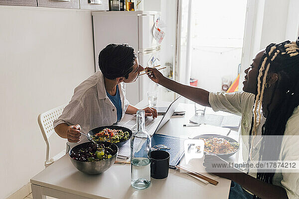 Young businesswoman feeding poke to girlfriend at home