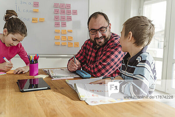 Lächelnder Nachhilfelehrer unterrichtet Jungen mit Buch am Tisch