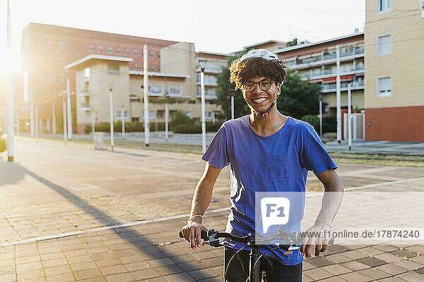 Happy man wearing helmet standing with bicycle in city