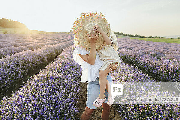 Mother and daughter covering face with hat in lavender field