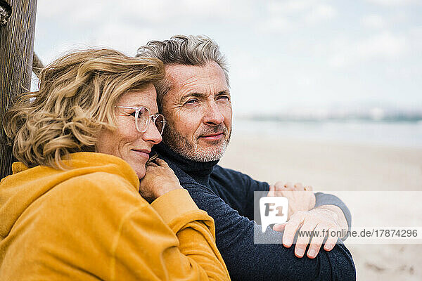 Lächelnde reife Frau mit Brille genießt den Urlaub mit Mann am Strand