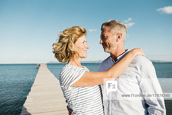 Smiling woman with man standing at jetty on sunny day