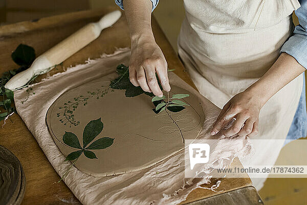 Hand of craftsperson removing leaf from clay at art studio