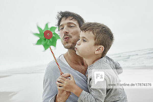 Father and son blowing green pinwheel on the beach