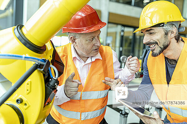 Male and female colleagues discussing robotic machine in industrial factory