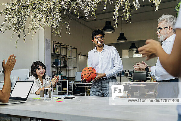 Colleagues congratulating businessman holding basketball at office