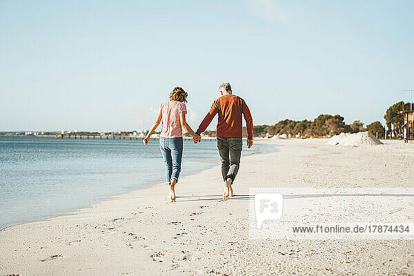Couple holding hands walking on shore at beach